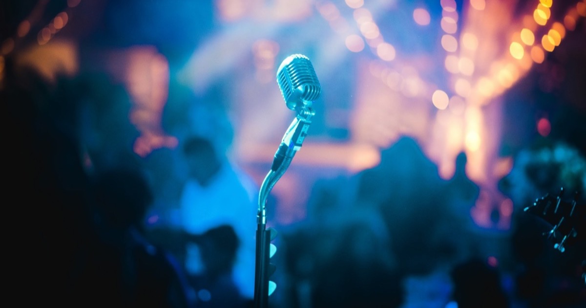 Vocalist performing on a darkened stage lit by blue and purple concert lighting