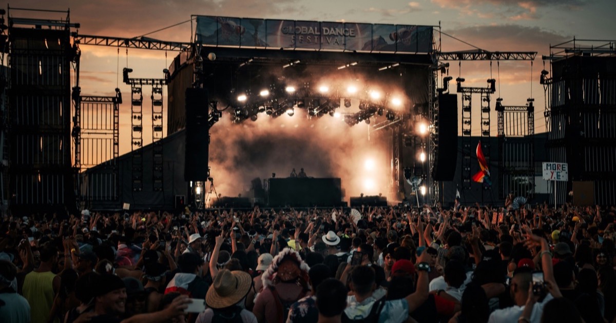 EDM festival crowd at night with stage lights and confetti over a packed main stage